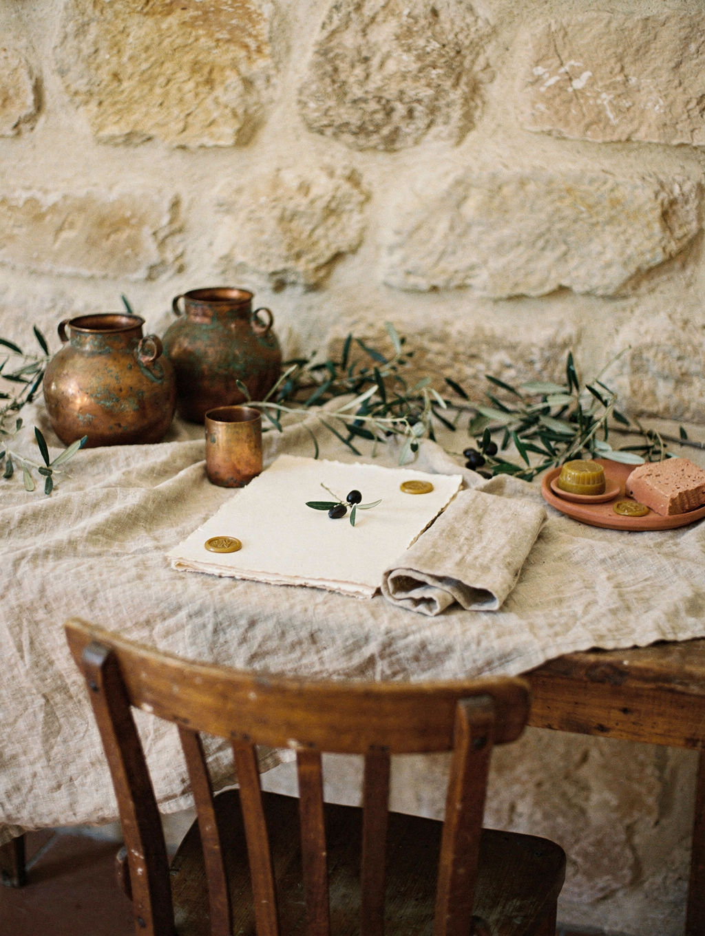 An empty wooden chair pulled up to a table set for one: linen, copper cup, a blank brief.