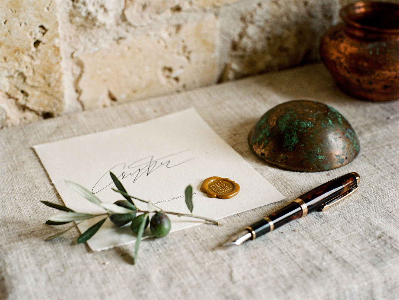 A signed counsel brief on linen with a copper paperweight, olive sprig, and beeswax seal.
